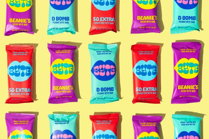 A flat lay of colorful Byte snack bar wrappers arranged in a neat grid on a yellow background