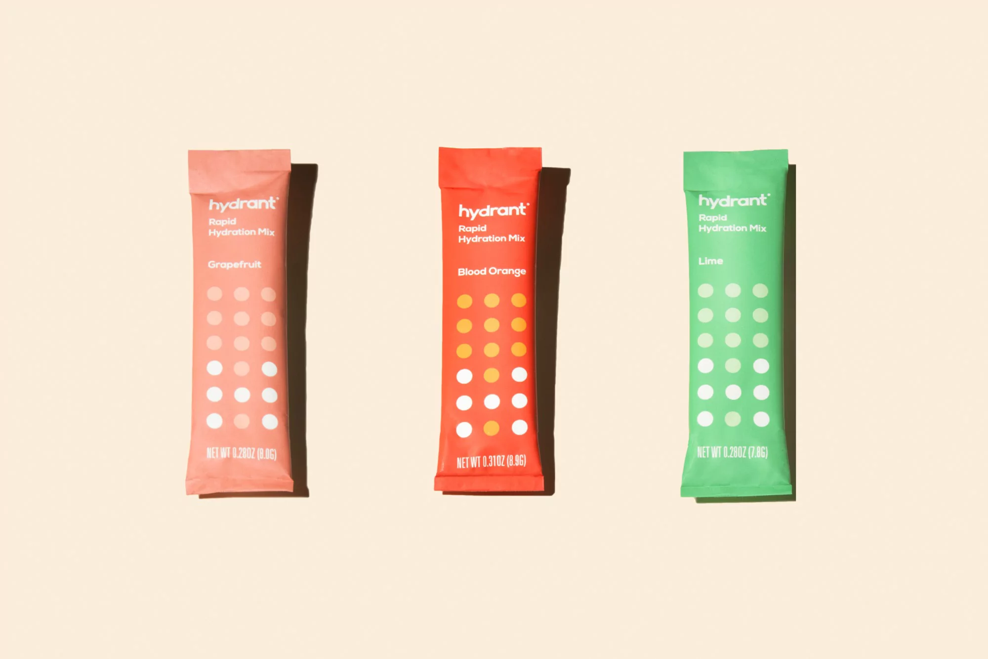 Three Hydrant Rapid Hydration Mix packets in grapefruit, blood orange, and lime flavors on a beige background, showcasing hydration products.