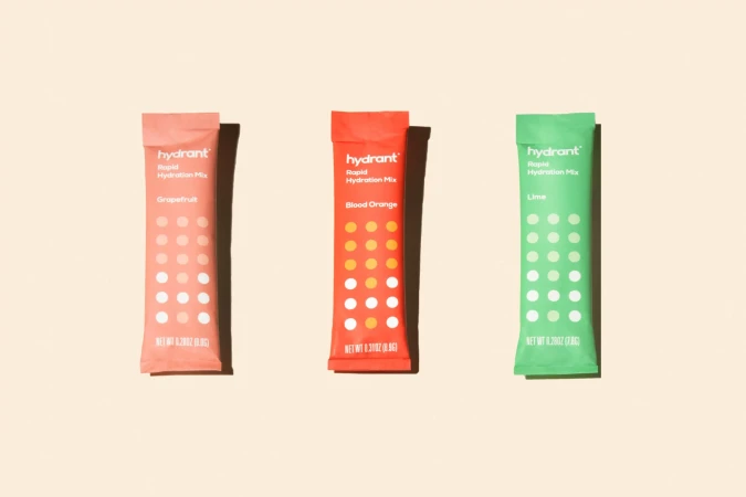 Three Hydrant Rapid Hydration Mix packets in grapefruit, blood orange, and lime flavors on a beige background, showcasing hydration products.