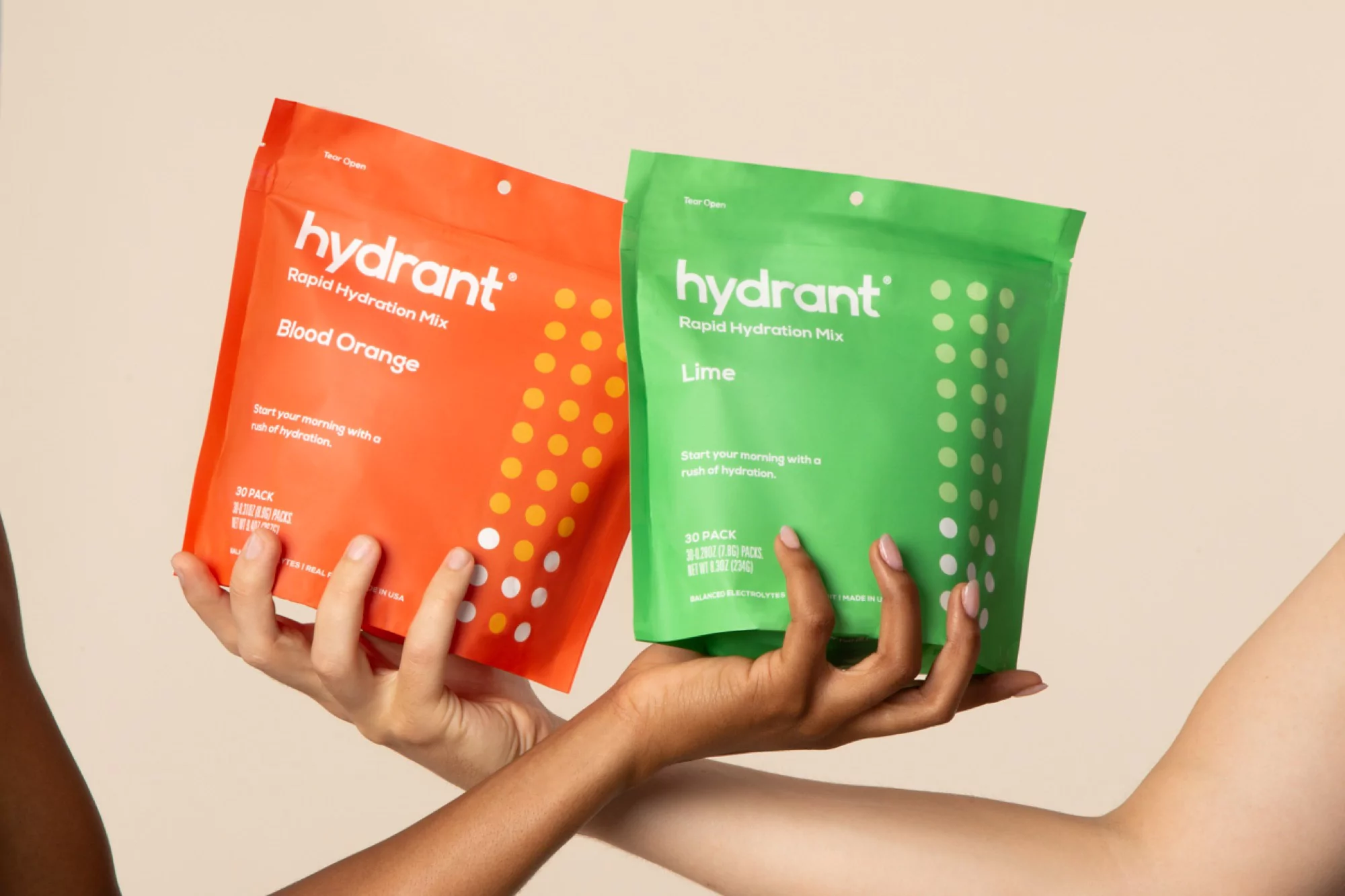 Two hands hold an orange and green hydration mix packet in a studio with soft lighting, close up shot. Hydration and wellness theme.