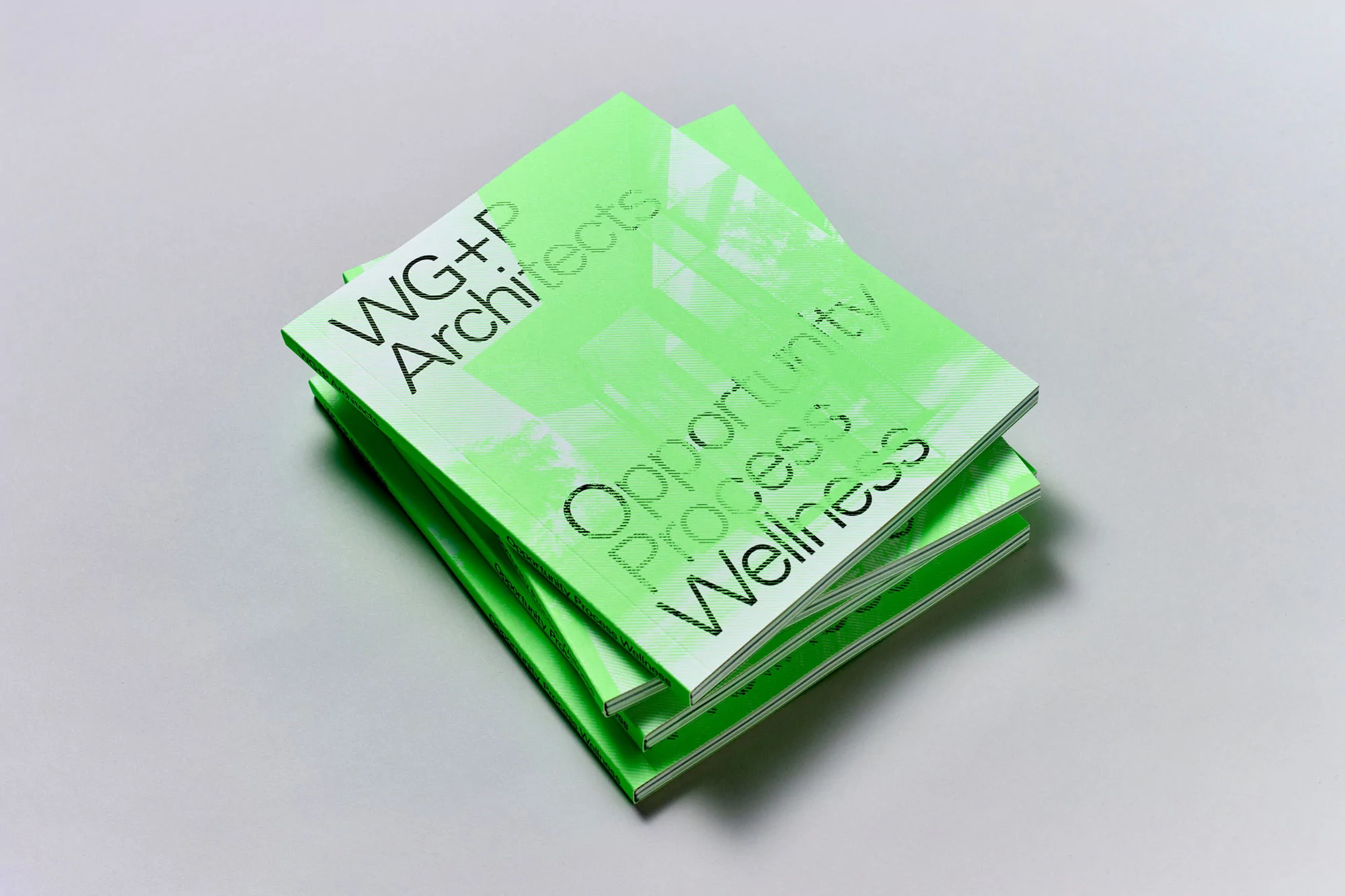 Stack of light-green architectural publications featuring the text 'WG+P Architects,' 'Opportunity, Process, Wellness' on a gray surface.