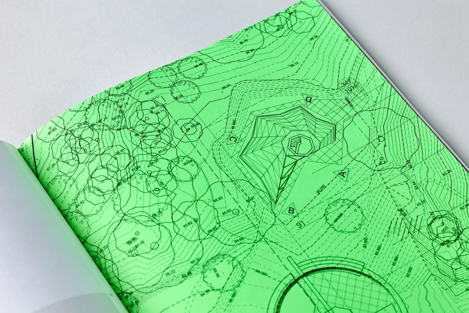 Architectural blueprint spread open, showcasing a detailed design in green ink on white paper; sharp focus on planning and design elements.