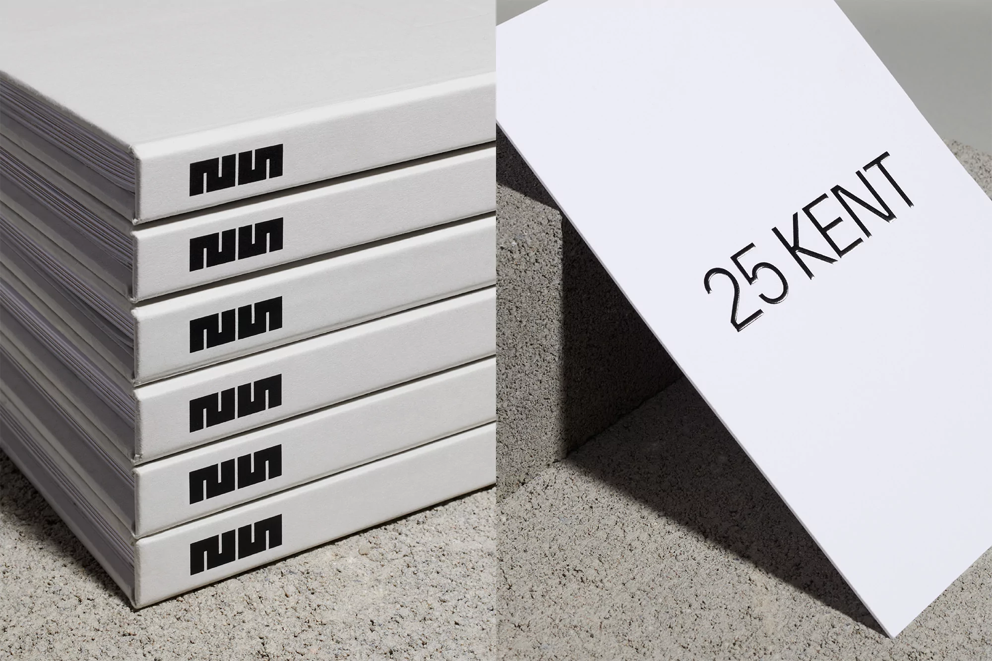 Stack of white books with black logo and white book with black text on grey surface in eye-level close-up.
