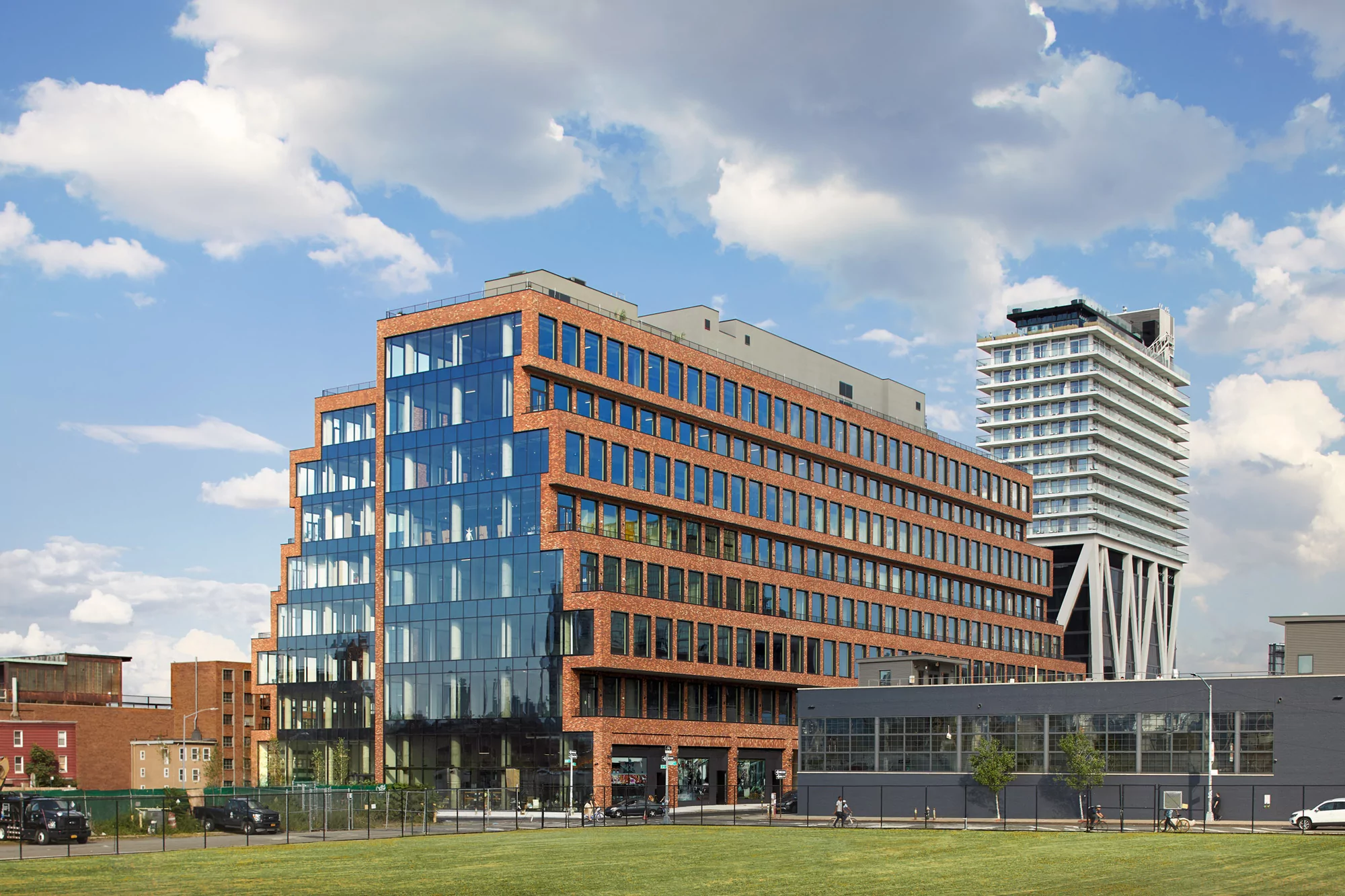 Exterior view of a modern, red brick office building with glass windows against a blue sky with clouds, reflecting urban architecture.