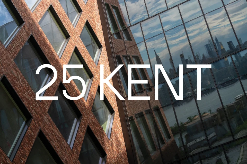 Exterior architecture shot of 25 Kent building featuring brick facade and glass windows with a city skyline reflection, daytime.