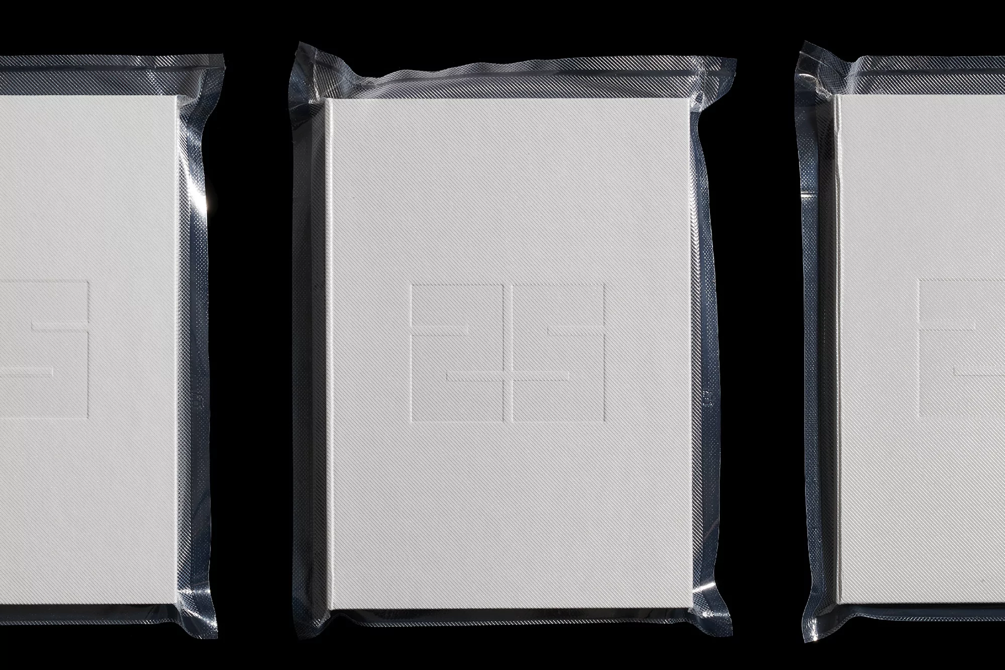 Three packaged white books are precisely arranged in a row against a dark backdrop, highlighting their clean design and textured covers.