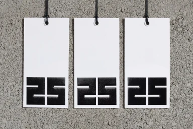 Three white vertical rectangular hang tags with black numeric print suspended against a textured concrete wall
