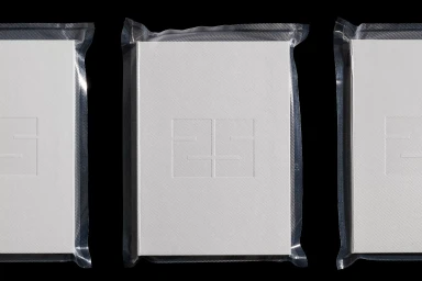 Three white books sealed tightly in clear plastic vacuum packaging against a solid black background.