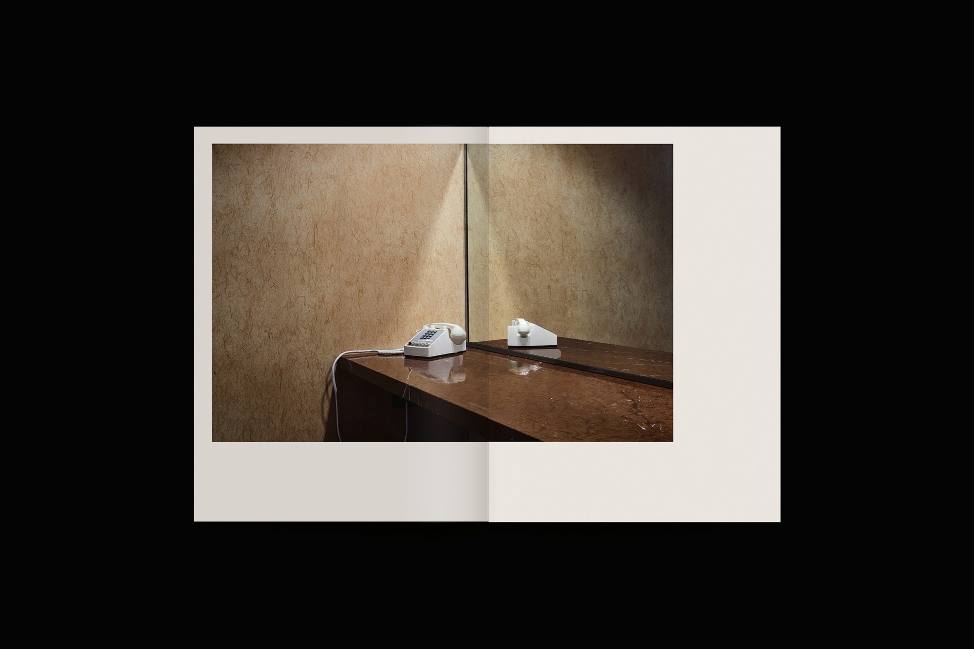 Retro white rotary phone on a wooden table with a mirror reflecting it against a tan textured wall, captured indoors.