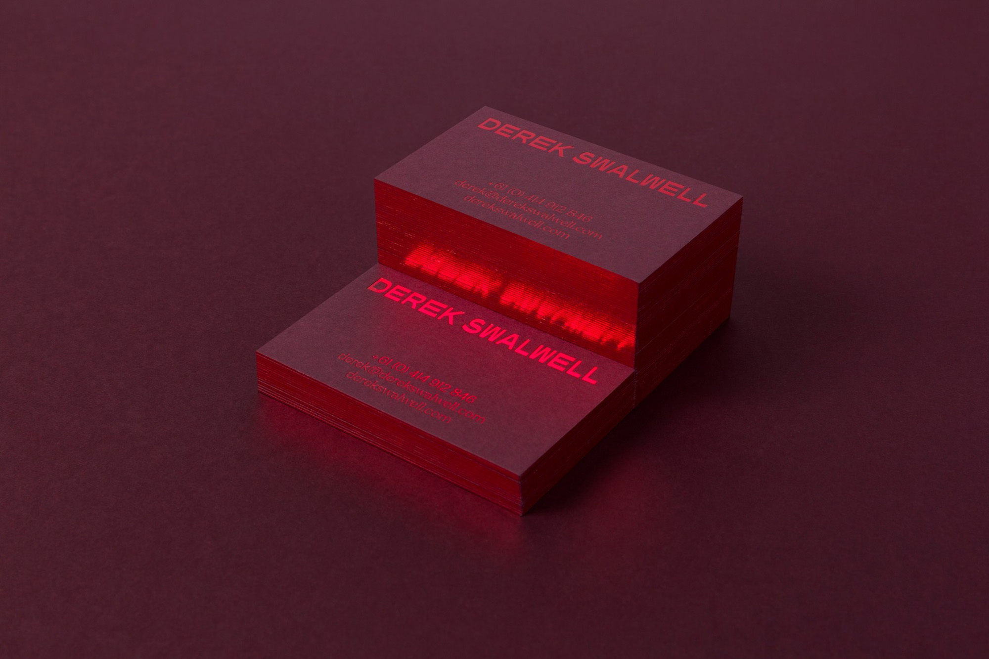 Elevated view of two stacks of crimson business cards with red text, placed on a dark red surface in a minimalist composition.