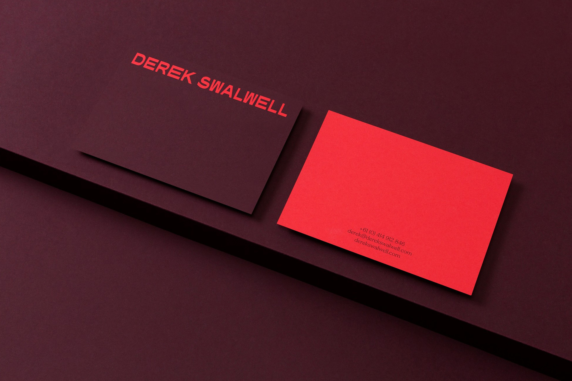 Two business cards, one dark red with red text and the other bright red, rest on a dark red surface with sharp angles.