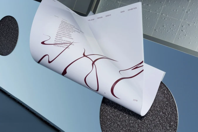 Curved white printed paper sheet with maroon typography against a blue and textured surface background