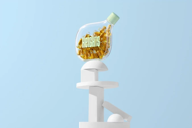 Clear bottle of golden capsules with the word HEIGHTS on white geometric stand against a baby blue background in a studio shot.