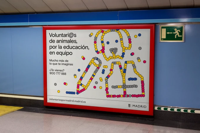 Advertisement in a subway station featuring a graphic of a dog and a pencil formed by colorful circles, promoting animal volunteering.