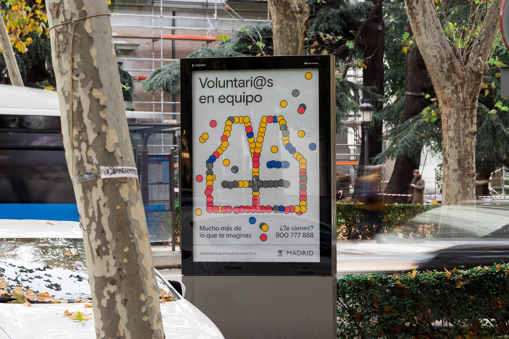 Outdoor advertising in Madrid, Spain features a colorful volunteer recruitment campaign. Illustration of a vest made of colored dots.