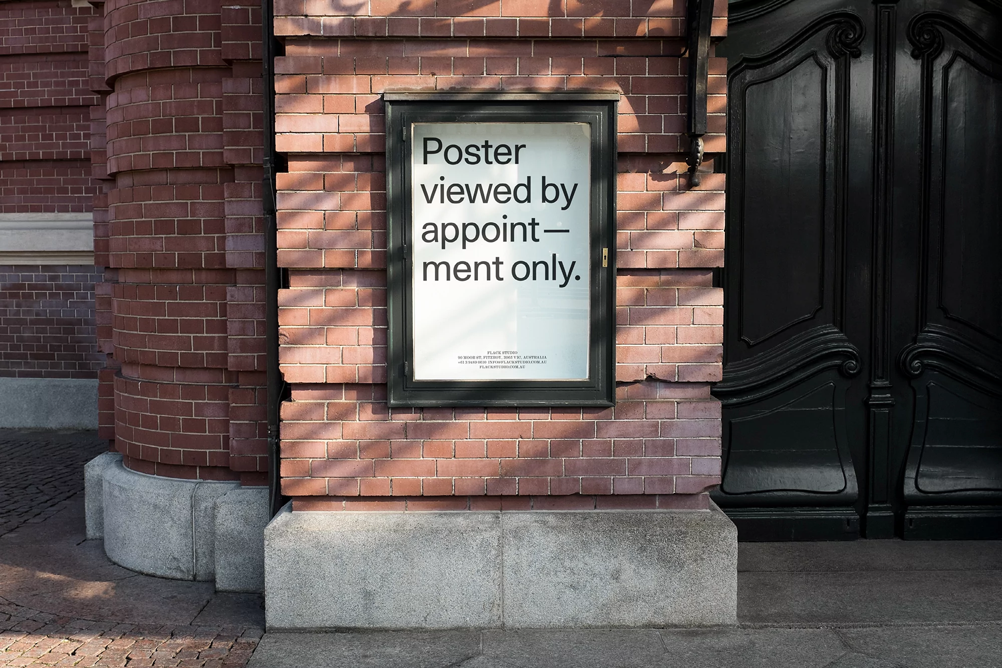 Poster displayed on a brick wall next to a dark, ornate door, viewed by appointment only, in natural light, creating a formal yet accessible mood.