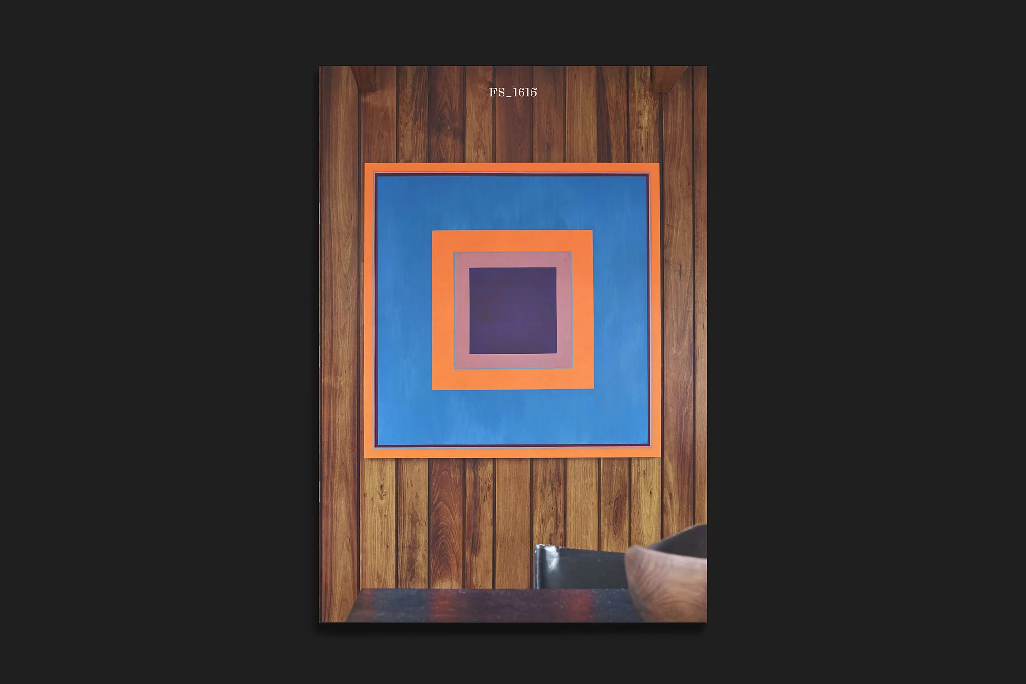 Abstract geometric art with concentric squares in blue, orange, lilac and purple hangs on a natural wood paneled wall above a dark table.