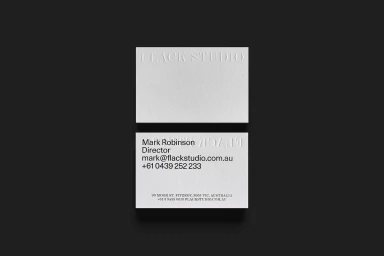 Two white business cards with embossed Flack Studio branding on a dark grey background.