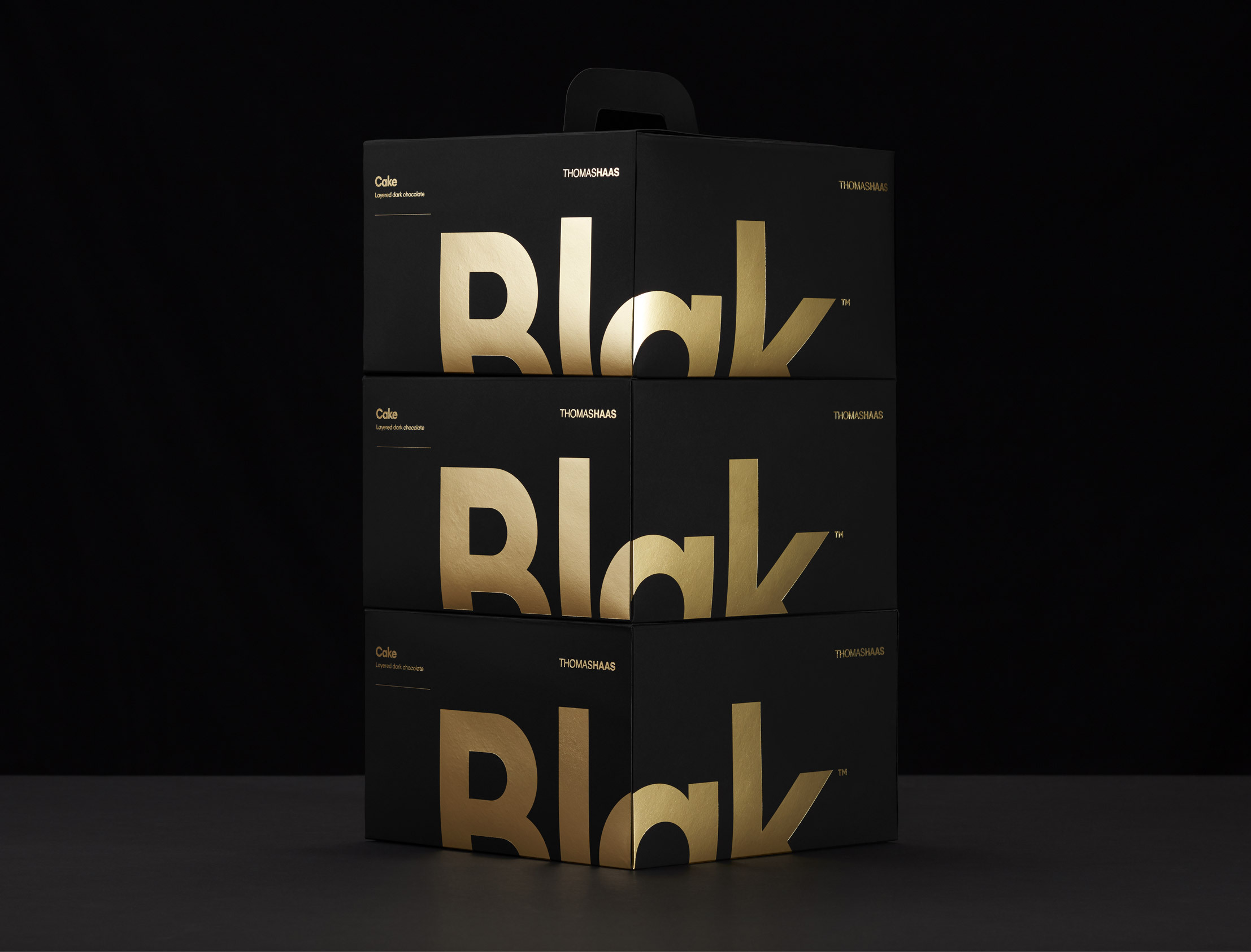 Three black boxes with gold text stacked on top of each other against a dark background, product shot, elegant design.
