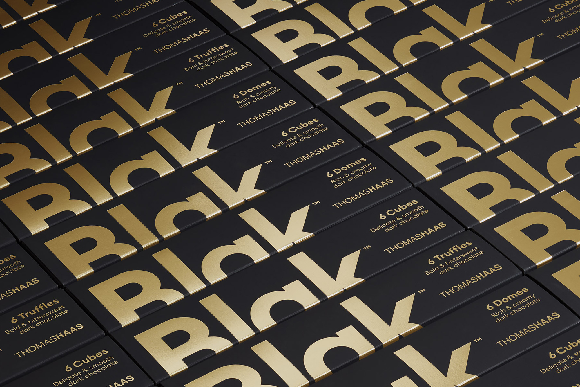 Close-up of black chocolate bar packaging with gold lettering arranged in a grid, highlighting the elegant product design and branding.