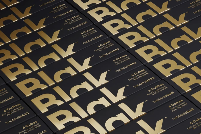 Close-up angled arrangement of black chocolate boxes featuring large metallic gold typographic branding.