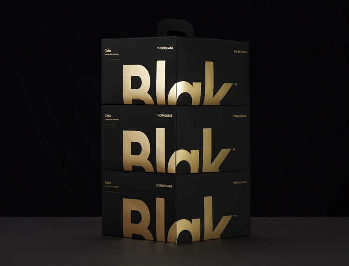 Three stacked black packaging boxes featuring large reflective gold typography spelling Blak against a dark backdrop.