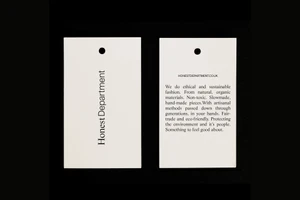 Two white paper swing tags with black typography against a dark background, showing brand name and ethical fashion statement text.