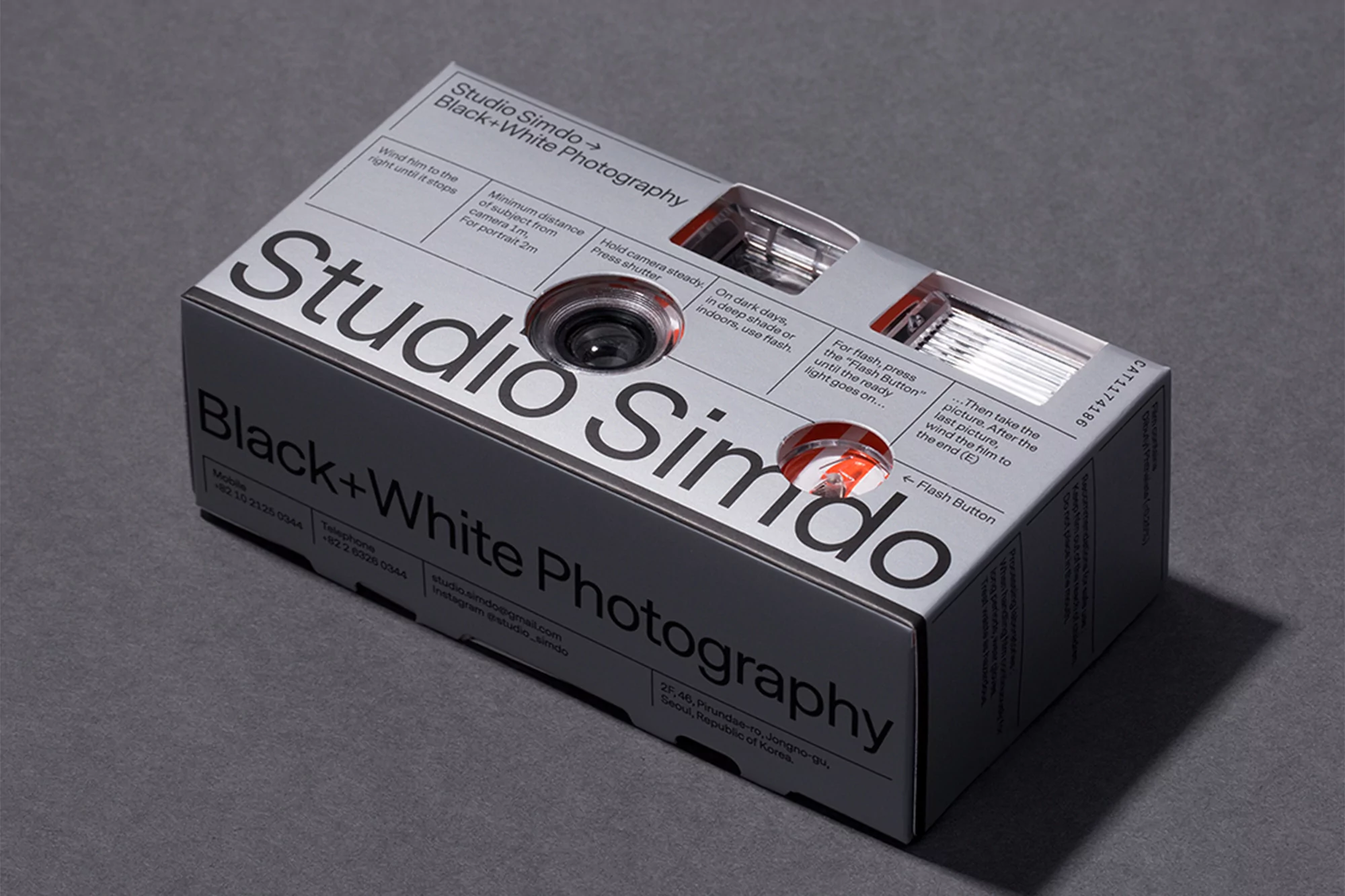 Studio Simdo black and white photography camera inside its packaging on a gray surface, showcasing the product's lens and design.