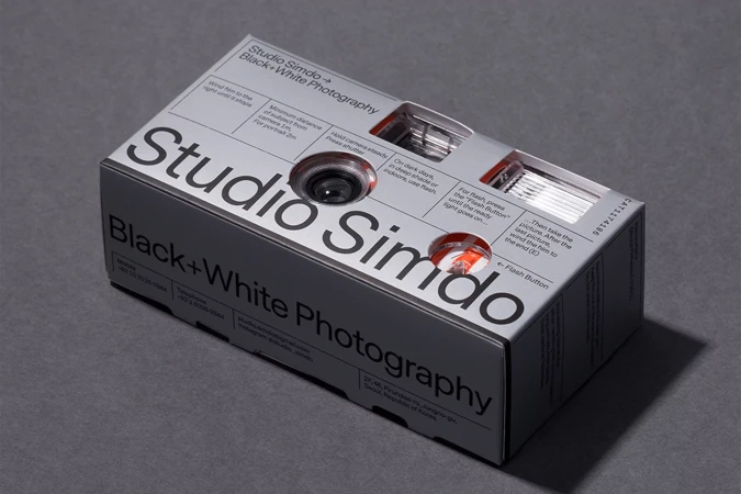 Studio Simdo black and white photography camera inside its packaging on a gray surface, showcasing the product's lens and design.