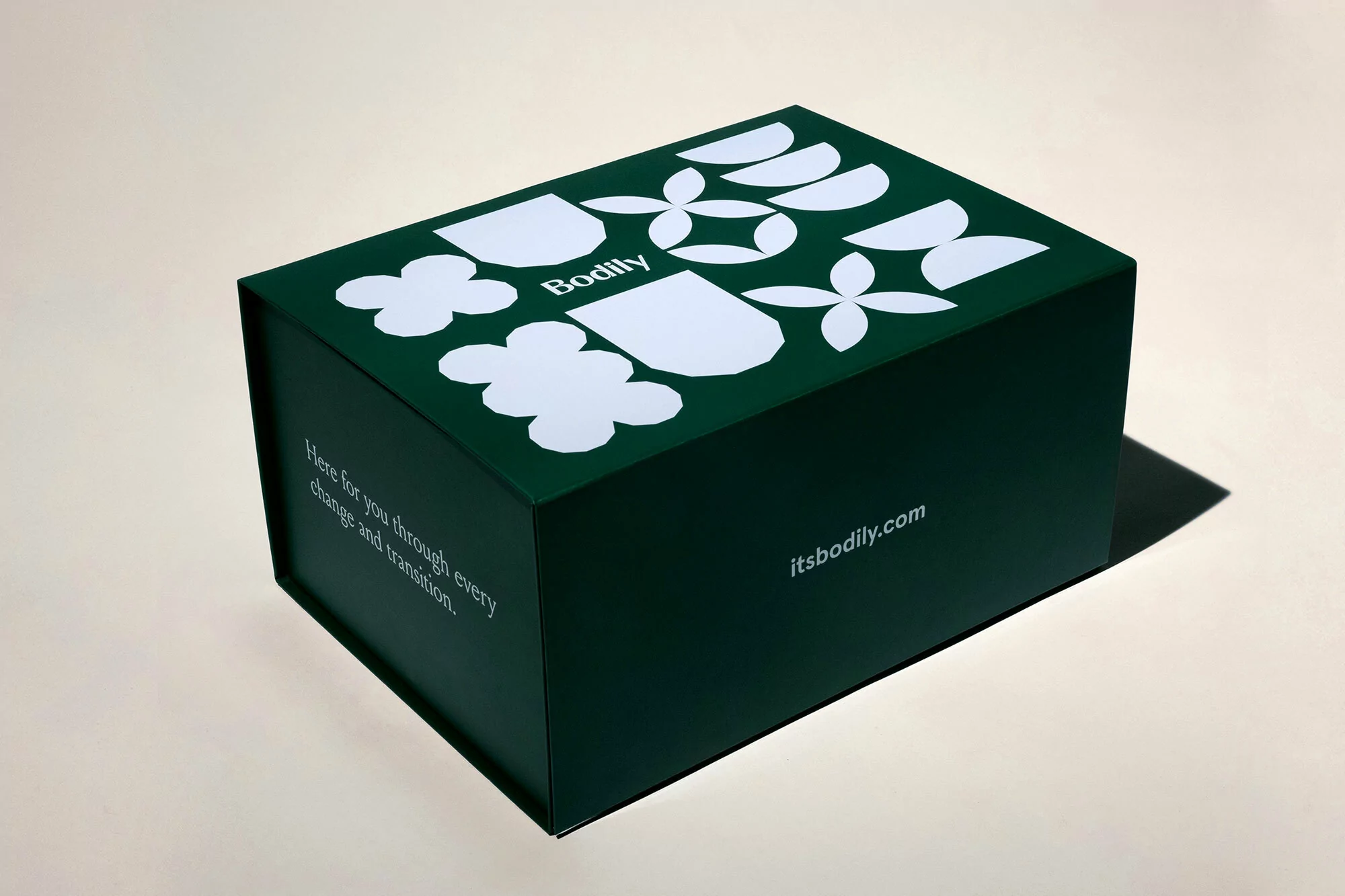 Angled studio shot of a dark green rectangular Bodily box with flower and geometric patterns, along with text on the front and side.