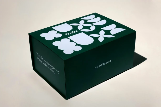 Angled studio shot of a dark green rectangular Bodily box with flower and geometric patterns, along with text on the front and side.