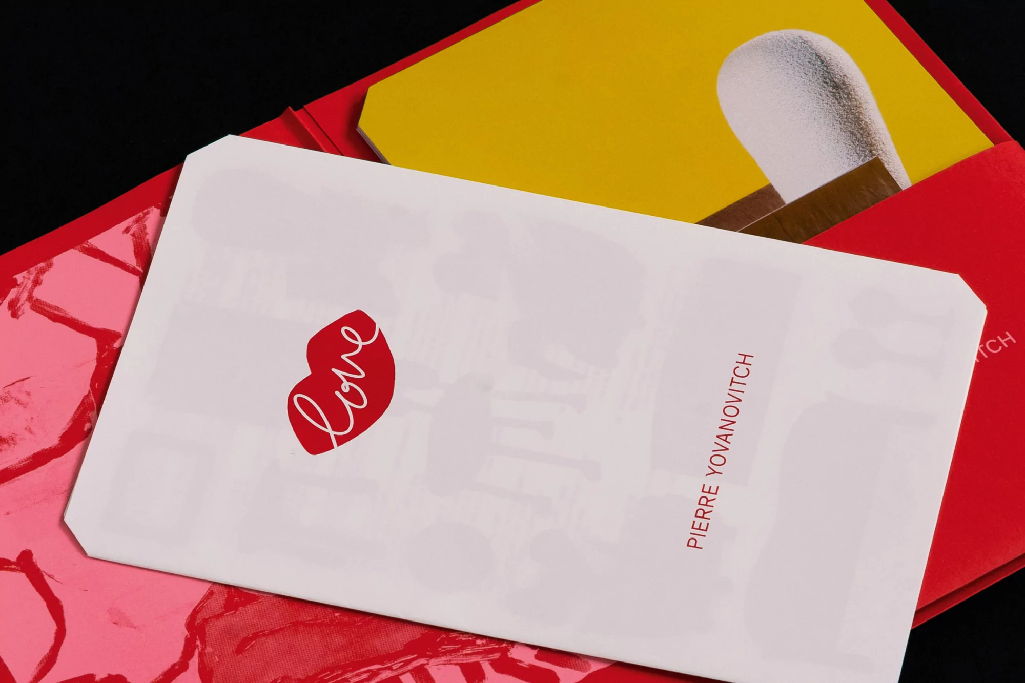 Envelope with a 'love' heart and 'Pierre Yovanovitch' text in a red and pink color scheme with a minimalist aesthetic.