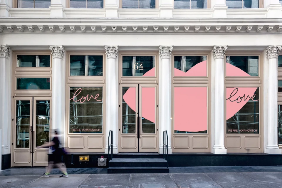 Storefront facade with modern design elements, pink heart accents, and a blurred pedestrian passing by in an urban environment.