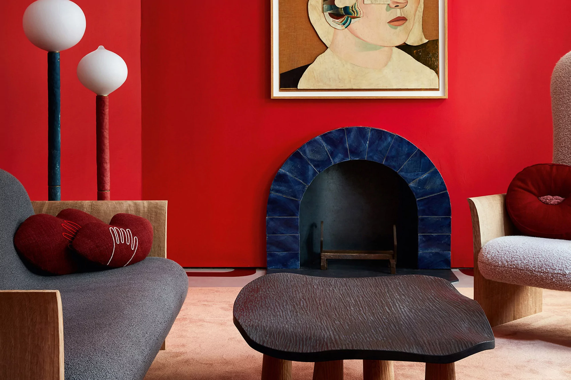 Stylish interior with gray couch, throw pillows, unique coffee table, modern art, and fireplace against vibrant red wall.