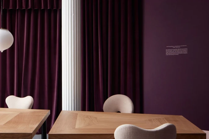 Interior design with wooden tables and upholstered chairs, set against a backdrop of plum-colored curtains and wall, soft lighting.