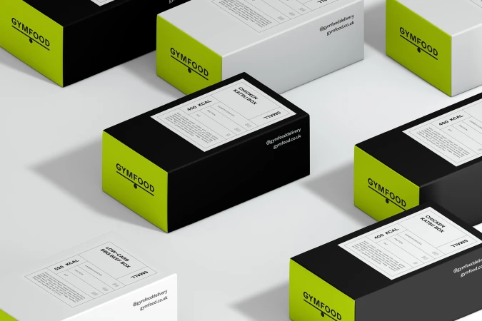Several black and white Gymfood meal boxes with nutritional information are arranged on a clean, white surface, food and beverage.