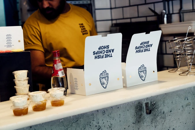 Fish and chips shop display featuring food containers, drink bottle, and branded packaging, showcasing culinary offerings in a casual setting.