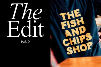 Close-up of a dark t-shirt with bold yellow text reading The Fish And Chips Shop alongside graphic typography reading The Edit Vol. 6