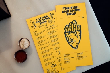 Bright yellow restaurant menus with black illustrations and two small metal condiment bowls on a light surface