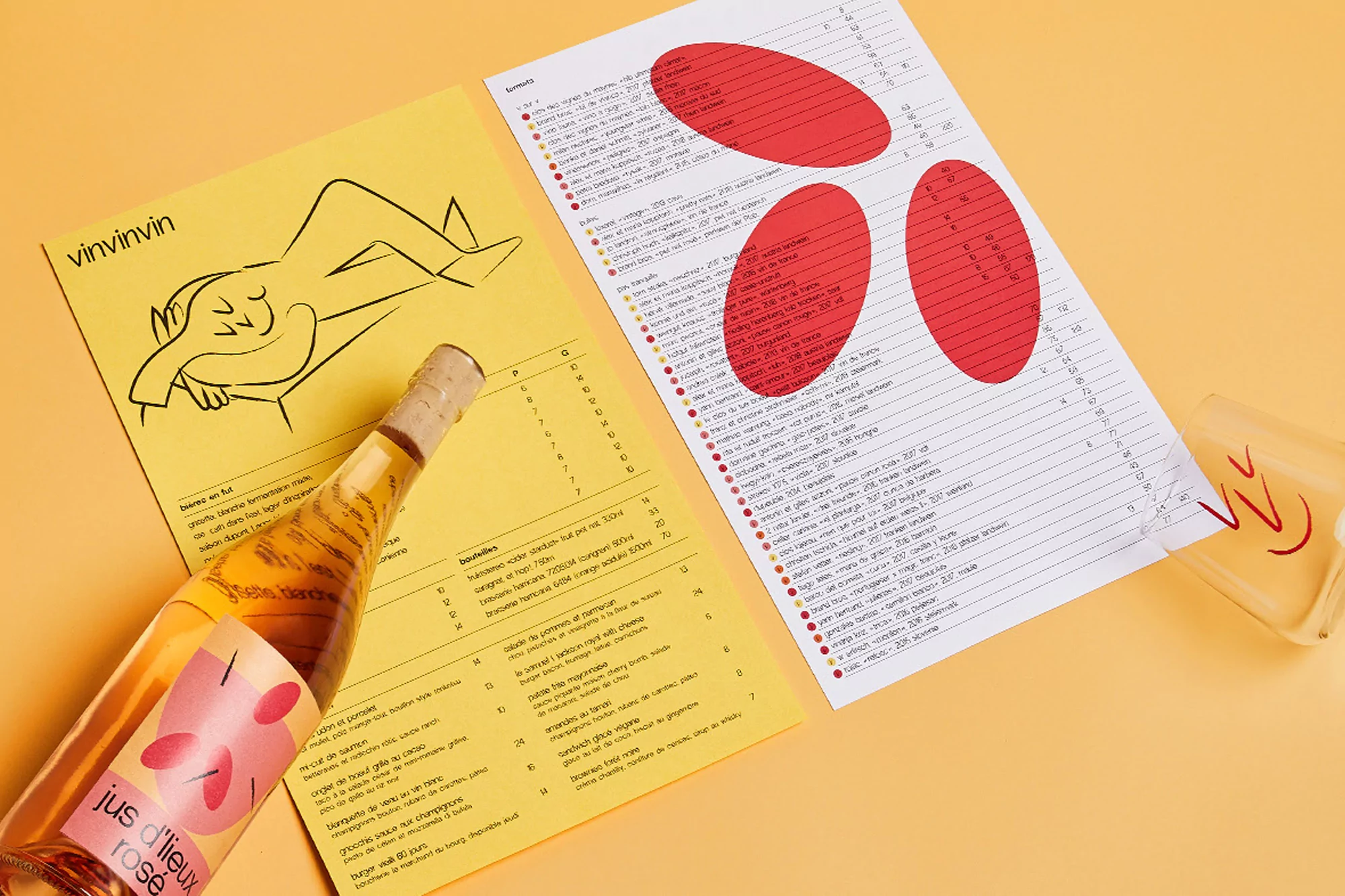 Flat lay of a bottle of rosé wine beside illustrated wine menus, all against a warm yellow background, suggesting a relaxed dining atmosphere.