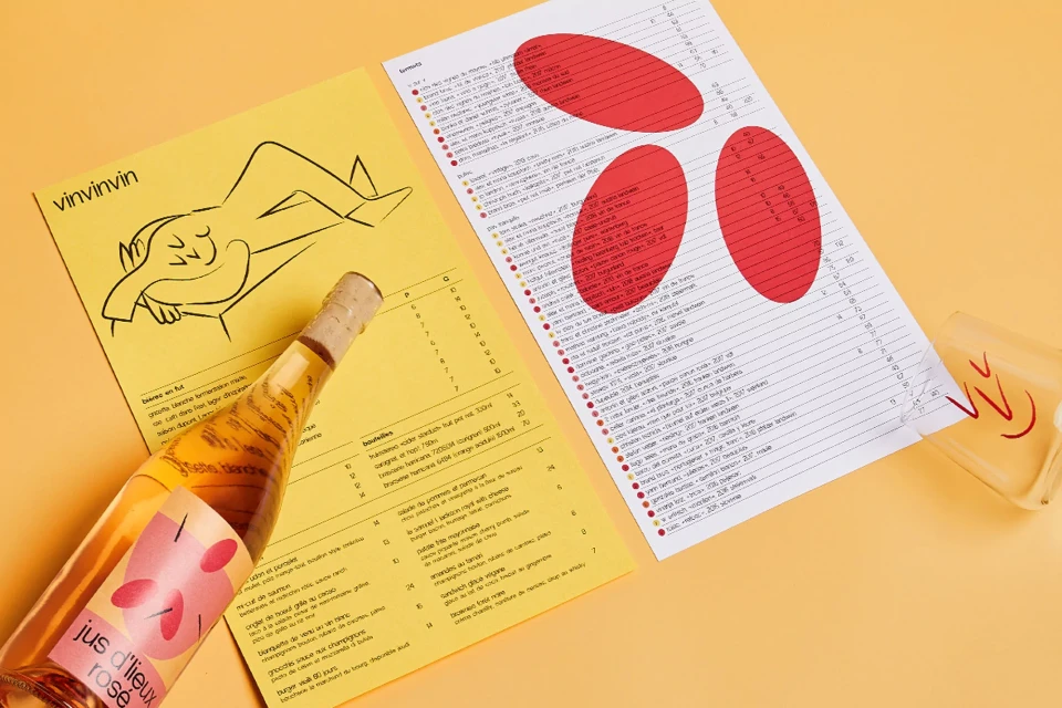 Flat lay of a bottle of rosé wine beside illustrated wine menus, all against a warm yellow background, suggesting a relaxed dining atmosphere.