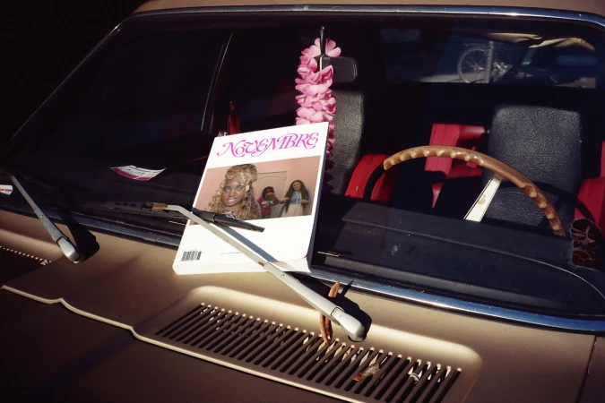 Vintage car hood displays a magazine cover with a portrait of a woman with blonde hair next to a pink floral decoration and black car interior.
