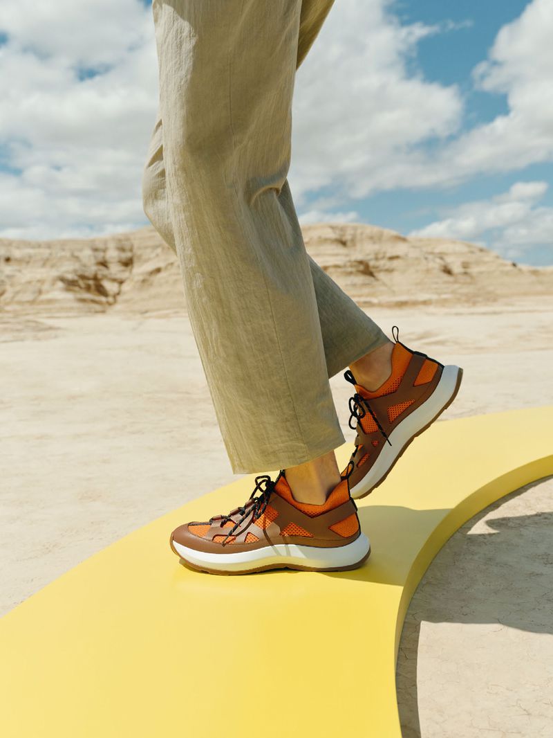 A low-angle shot showcasing a person wearing brown athletic shoes with khaki trousers, standing on a yellow surface, with a desert landscape backdrop.