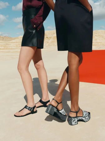 Two fashion models showcase contemporary sandals in a desert-like setting, highlighting modern style and footwear design against a neutral backdrop.