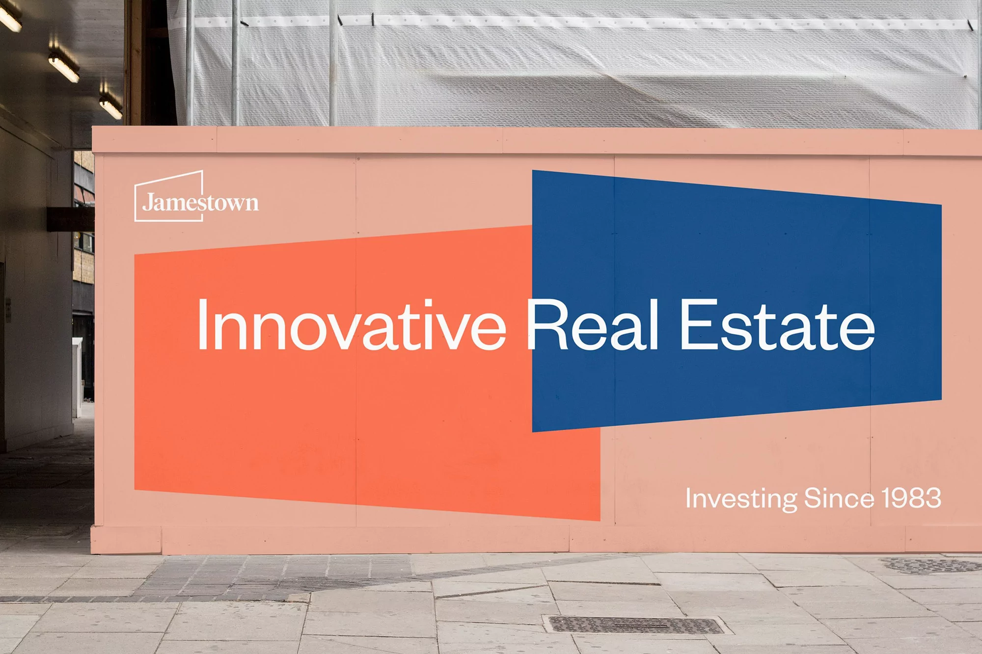 Building hoarding with real estate advertisement featuring Jamestown logo, coral and blue geometric shapes, and the text Innovative Real Estate.