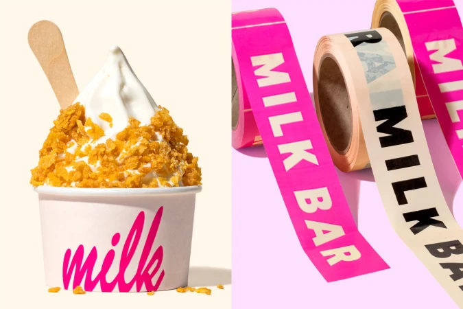 Close-up studio shot of a paper cup with 'milk' written on it, filled with soft serve ice cream topped with cereal, and rolls of Milk Bar tape.