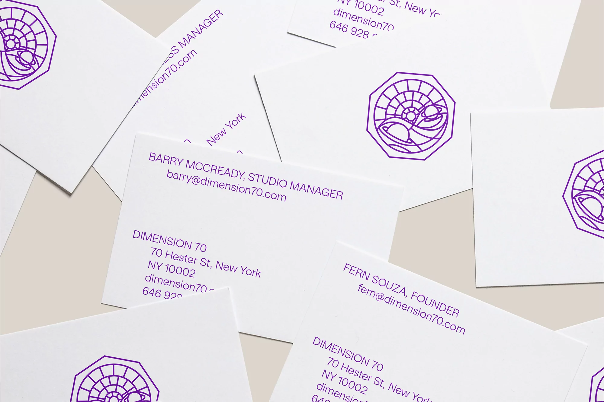 Pile of white business cards with purple logo and text, arranged on a light beige surface, featuring Dimension 70 contact information.