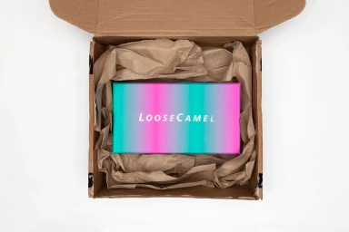 An open cardboard shipping box containing crumpled brown packing paper and a colorful branded product box.