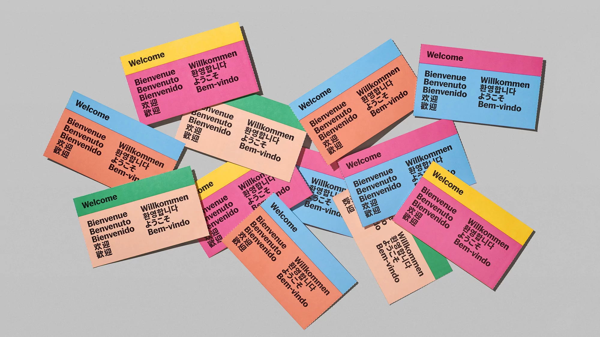 Collection of colorful cards printed with "Welcome" in multiple languages, set against a neutral background in a studio environment.