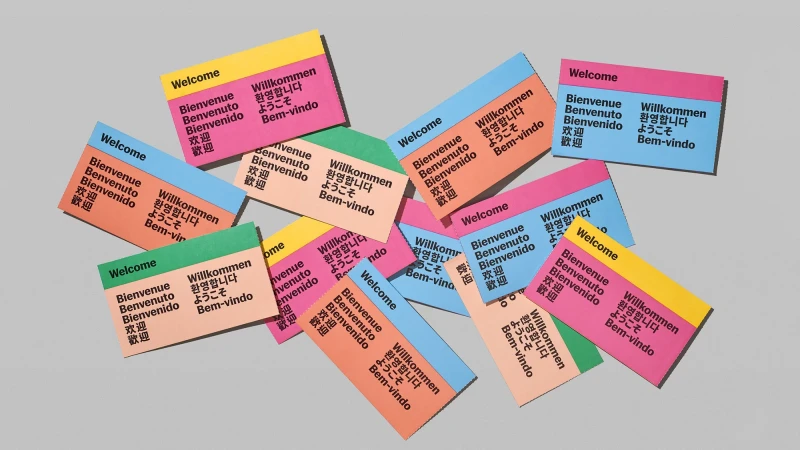 Collection of colorful cards printed with "Welcome" in multiple languages, set against a neutral background in a studio environment.